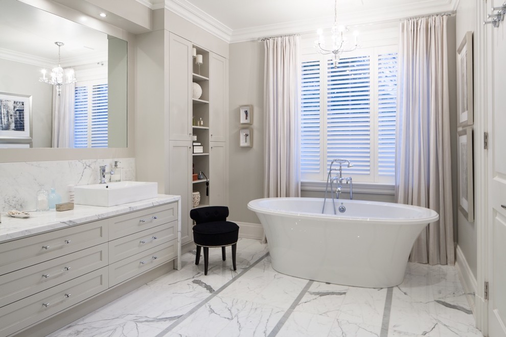 Idée de décoration pour une salle de bain principale design avec un plan de toilette en marbre, un sol en marbre, une vasque, une baignoire indépendante, un placard avec porte à panneau encastré, des portes de placard beiges et un mur beige.