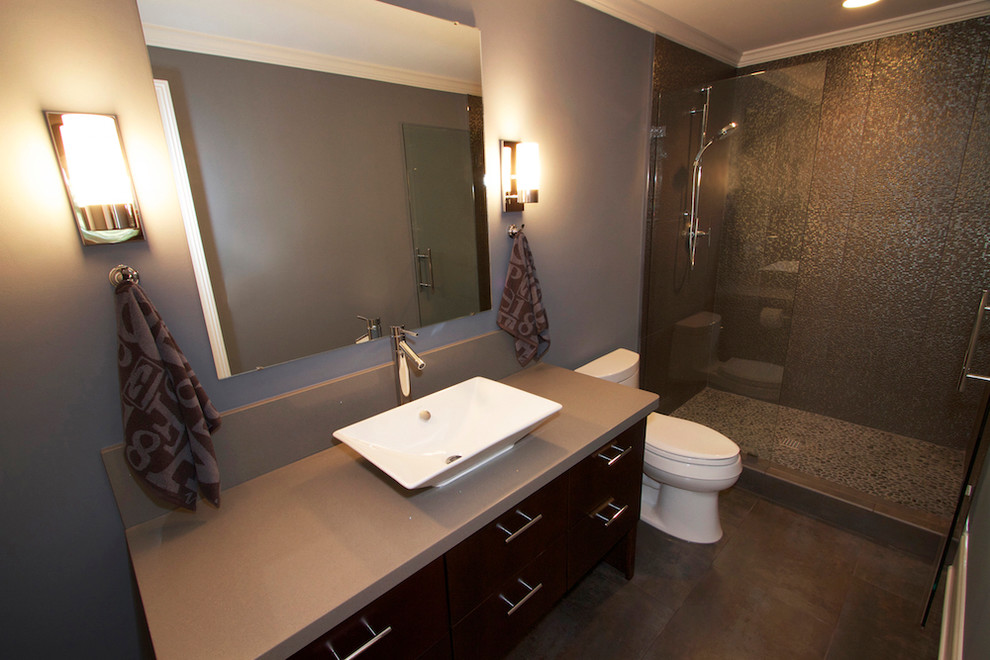 Exemple d'une salle de bain moderne en bois foncé de taille moyenne avec un placard à porte plane, WC à poser, un mur gris, une vasque, un plan de toilette en surface solide, une cabine de douche à porte battante, un sol en carrelage de porcelaine et un sol gris.