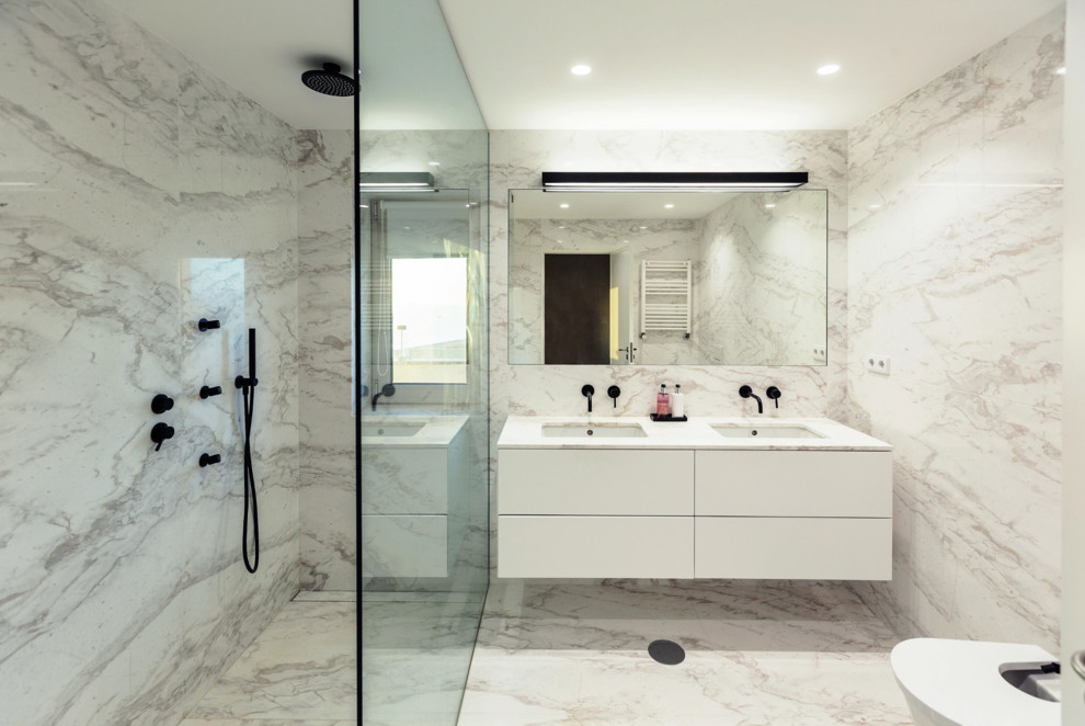 Idéer för att renovera ett mellanstort funkis vit vitt en-suite badrum, med släta luckor, vita skåp, en dusch i en alkov, en vägghängd toalettstol, grå kakel, vit kakel, marmorkakel, vita väggar, marmorgolv, ett undermonterad handfat, bänkskiva i kvarts, grått golv och med dusch som är öppen