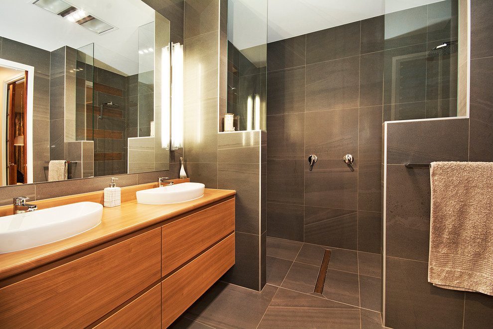 Свежая идея для дизайна: ванная комната в современном стиле с светлыми деревянными фасадами, открытым душем, унитазом-моноблоком, серой плиткой, керамогранитной плиткой, полом из керамогранита, накладной раковиной и столешницей из ламината - отличное фото интерьера