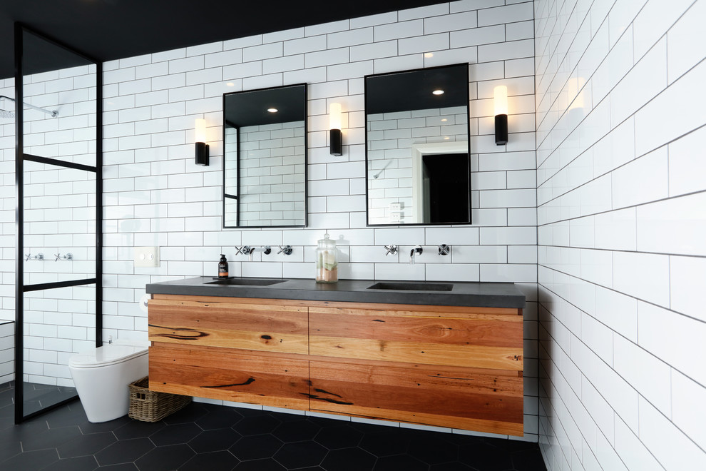 Свежая идея для дизайна: главная ванная комната в современном стиле с плоскими фасадами, унитазом-моноблоком, белой плиткой, керамической плиткой, белыми стенами, монолитной раковиной, черным полом, черной столешницей, фасадами цвета дерева среднего тона, ванной в нише, душевой комнатой, столешницей из бетона и открытым душем - отличное фото интерьера