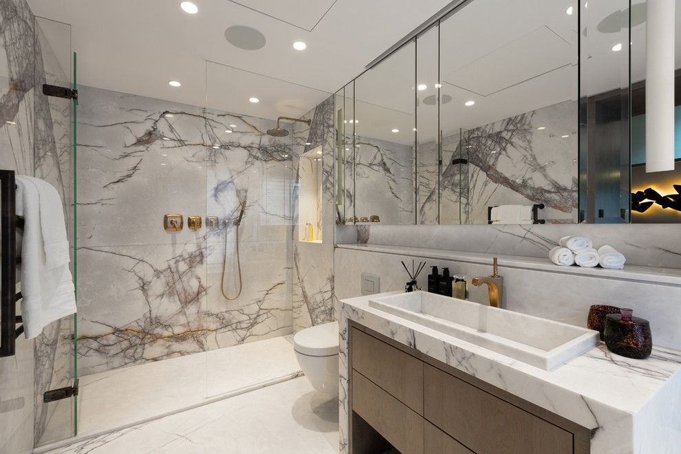 Idée de décoration pour une salle de bain design avec un placard à porte plane, des portes de placard marrons, WC suspendus, du carrelage en marbre, un mur gris, un lavabo posé, un plan de toilette en marbre, un sol blanc et une cabine de douche à porte battante.