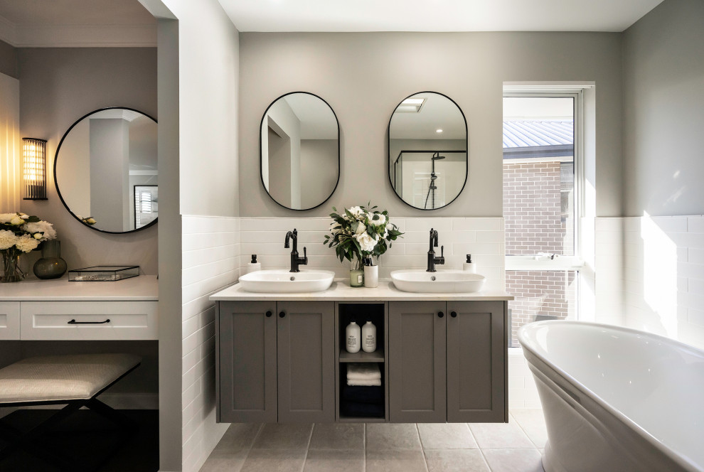 Cette image montre une salle de bain principale traditionnelle avec un placard à porte shaker, des portes de placard grises, une baignoire indépendante, un carrelage blanc, un carrelage métro, un mur gris, une vasque, un sol gris, un plan de toilette blanc, meuble double vasque et meuble-lavabo suspendu.