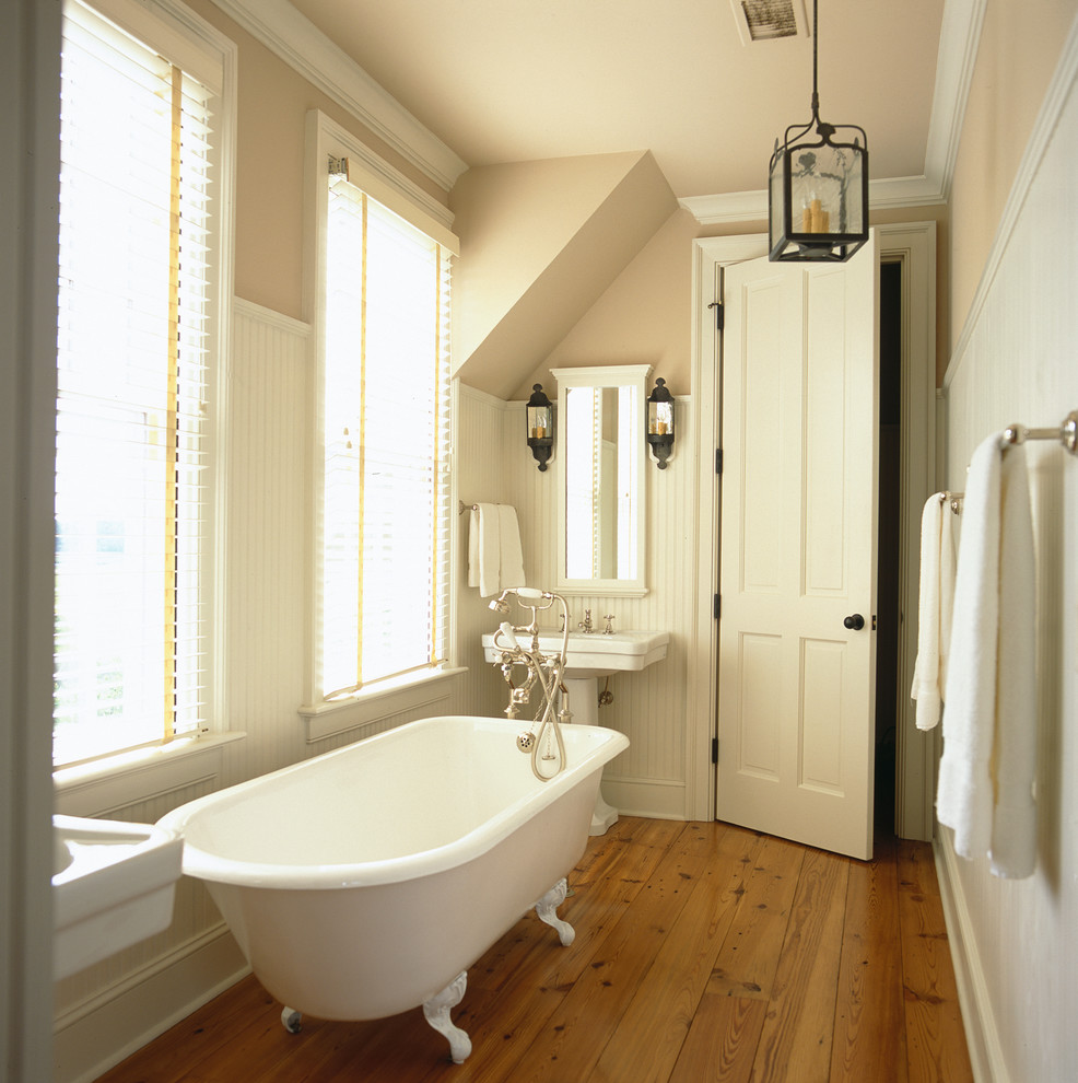 Ejemplo de cuarto de baño principal y largo y estrecho de estilo de casa de campo de tamaño medio con lavabo con pedestal, bañera con patas, paredes beige y suelo de madera en tonos medios