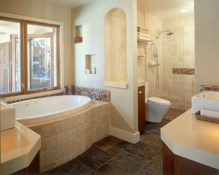 This is an example of a classic bathroom in San Diego with a vessel sink, flat-panel cabinets, medium wood cabinets, solid surface worktops, a built-in bath, a built-in shower, brown tiles and stone tiles.