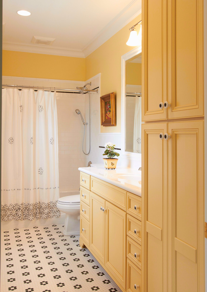 Idée de décoration pour une grande salle d'eau tradition avec un mur jaune, un placard avec porte à panneau encastré, des portes de placard jaunes, une baignoire en alcôve, un combiné douche/baignoire, un carrelage blanc, un carrelage métro, un sol en carrelage de céramique, un lavabo intégré, un plan de toilette en surface solide, un sol multicolore et une cabine de douche avec un rideau.