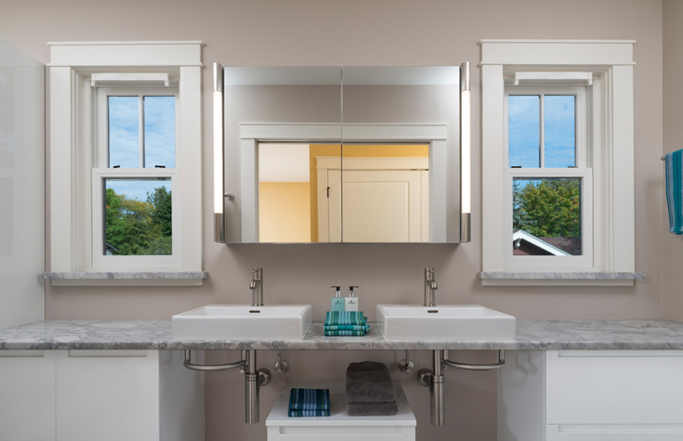 Cette photo montre une grande salle de bain principale tendance avec un placard à porte plane, des portes de placard blanches, un mur beige, une vasque et un plan de toilette en marbre.