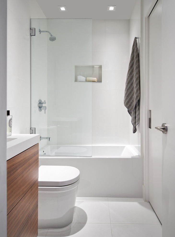 Photo of a small modern ensuite bathroom in San Francisco with flat-panel cabinets, dark wood cabinets, an alcove bath, a shower/bath combination, a one-piece toilet, white tiles, ceramic tiles, white walls, ceramic flooring, an integrated sink, engineered stone worktops, white floors, a hinged door and white worktops.