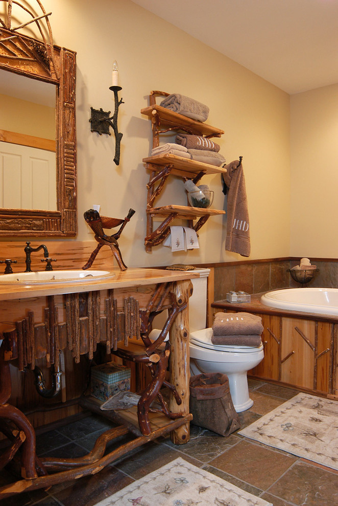 Cette photo montre une salle de bain montagne en bois brun de taille moyenne avec un lavabo encastré, un placard en trompe-l'oeil, un plan de toilette en bois, une baignoire posée, WC à poser, un carrelage marron, des carreaux de céramique, un mur jaune et un sol en carrelage de céramique.