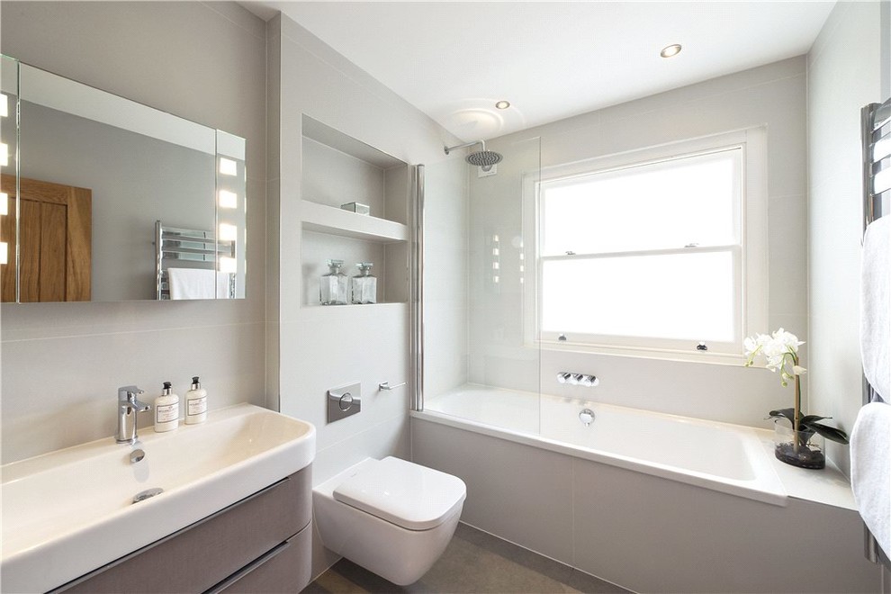Photo of a medium sized contemporary ensuite bathroom in Oxfordshire with a built-in bath, a shower/bath combination, a wall mounted toilet, grey tiles, porcelain tiles, grey walls, porcelain flooring and a wall-mounted sink.