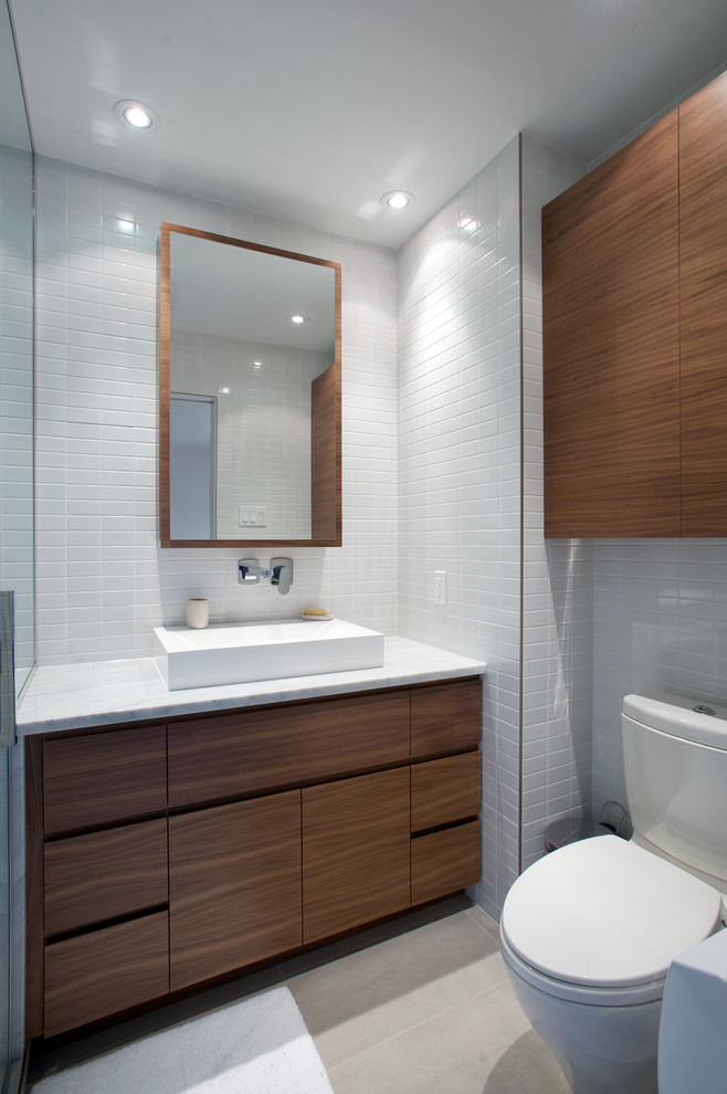 Mittelgroßes Modernes Badezimmer mit Aufsatzwaschbecken, flächenbündigen Schrankfronten, hellbraunen Holzschränken, Toilette mit Aufsatzspülkasten, weißen Fliesen, weißer Wandfarbe, Marmor-Waschbecken/Waschtisch und Keramikboden in Montreal