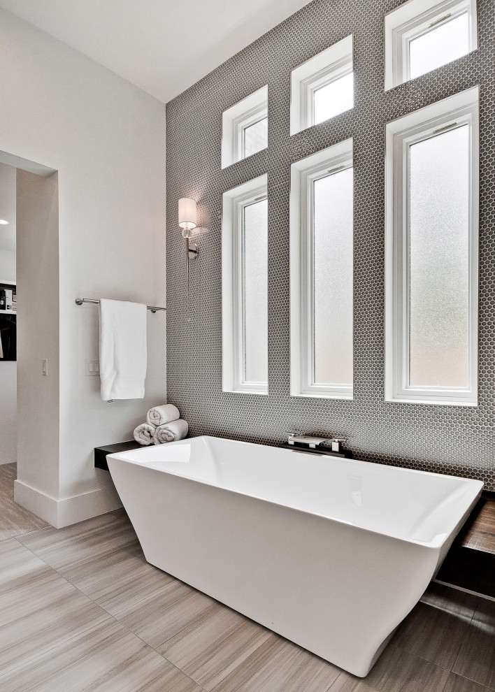 На фото: большая главная ванная комната в стиле модернизм с фасадами с выступающей филенкой, белыми фасадами, отдельно стоящей ванной, открытым душем, раздельным унитазом, серой плиткой, керамогранитной плиткой, серыми стенами, полом из керамогранита, раковиной с несколькими смесителями, столешницей из гранита, серым полом, душем с распашными дверями, черной столешницей, тумбой под две раковины и подвесной тумбой