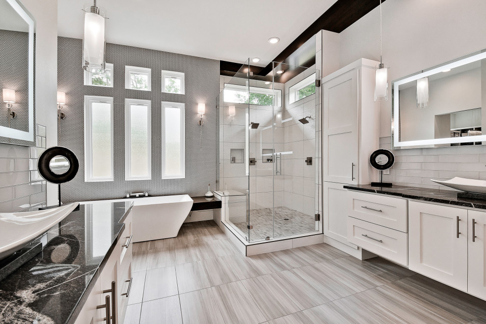 Inredning av ett modernt stort svart svart en-suite badrum, med luckor med upphöjd panel, vita skåp, ett fristående badkar, en öppen dusch, en toalettstol med separat cisternkåpa, porslinskakel, grå väggar, klinkergolv i porslin, grått golv, dusch med gångjärnsdörr, grå kakel, ett avlångt handfat och granitbänkskiva