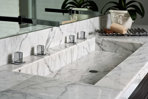 Immagine di una stanza da bagno design con ante nere, lavabo integrato e top in marmo