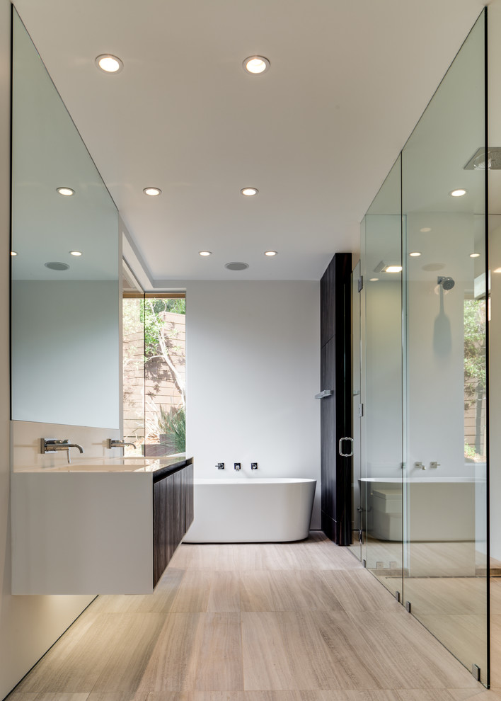 Modern inredning av ett badrum med dusch, med släta luckor, skåp i mörkt trä, ett fristående badkar, en kantlös dusch, vita väggar, ett integrerad handfat, beiget golv och dusch med gångjärnsdörr