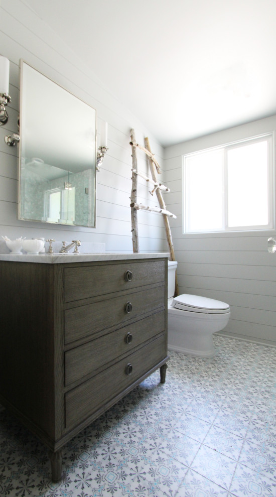Exemple d'une petite salle de bain bord de mer en bois brun avec un placard en trompe-l'oeil, WC séparés, un carrelage gris, une plaque de galets, un mur gris, un sol en marbre, un lavabo encastré, un plan de toilette en marbre, un sol multicolore, une cabine de douche à porte battante, un plan de toilette blanc, un banc de douche, meuble simple vasque, meuble-lavabo sur pied et du lambris de bois.