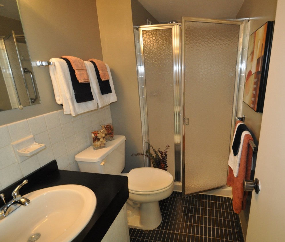 Bild på ett mellanstort 50 tals badrum med dusch, med släta luckor, vita skåp, en dusch i en alkov, en toalettstol med separat cisternkåpa, svart kakel, vit kakel, keramikplattor, beige väggar, klinkergolv i keramik, ett nedsänkt handfat och bänkskiva i akrylsten