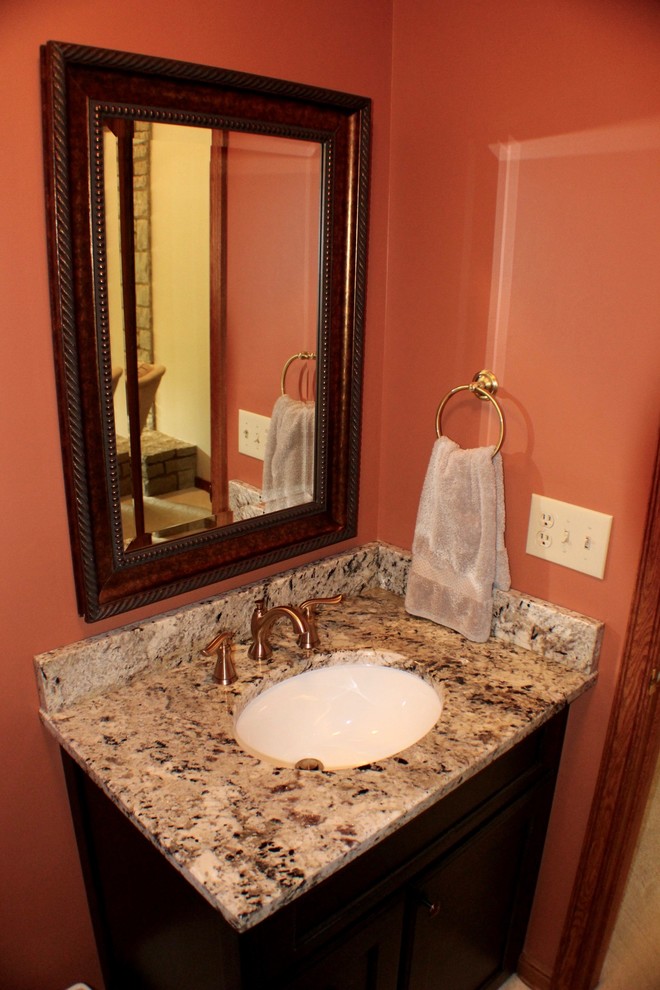 Cette image montre une petite salle d'eau traditionnelle en bois foncé avec un placard avec porte à panneau surélevé, WC à poser, un mur orange, un sol en bois brun, un lavabo encastré, un plan de toilette en granite et un sol marron.