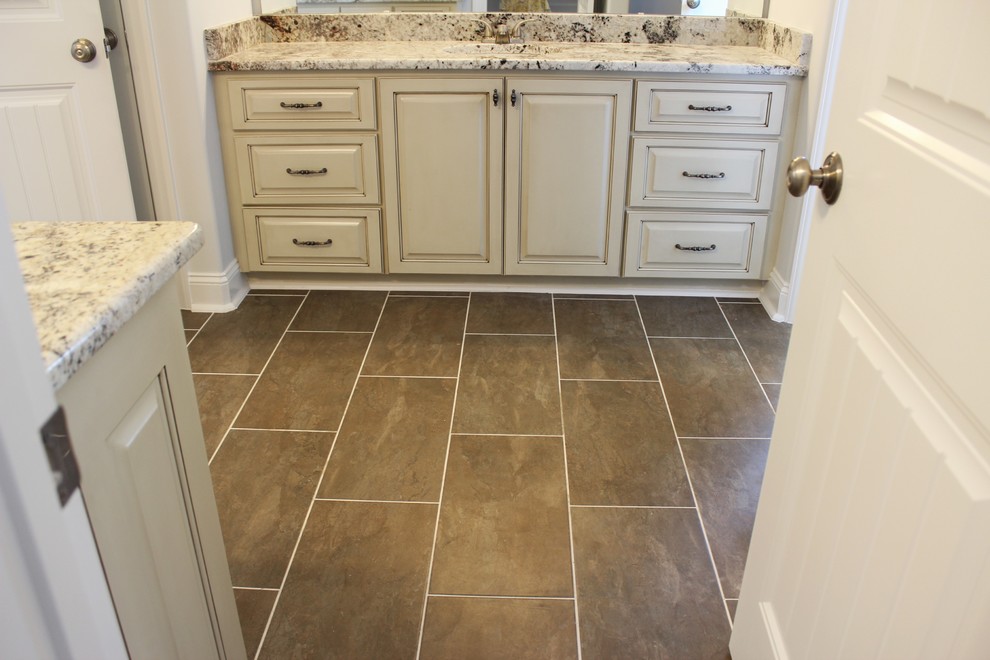 Large classic ensuite bathroom in Raleigh with raised-panel cabinets, distressed cabinets, a built-in shower, a one-piece toilet, brown tiles, porcelain tiles, white walls, ceramic flooring, a submerged sink and granite worktops.