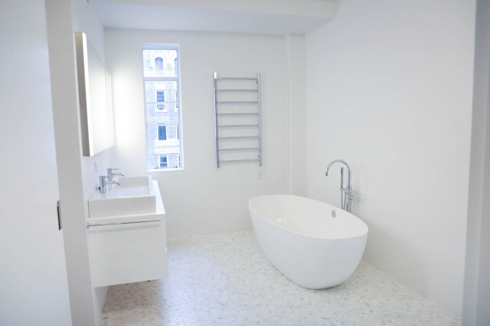 Photo of a large modern ensuite bathroom in New York with flat-panel cabinets, white cabinets, a freestanding bath, white tiles, ceramic tiles, mosaic tile flooring, a wall-mounted sink, engineered stone worktops, white floors, white worktops, double sinks and a floating vanity unit.