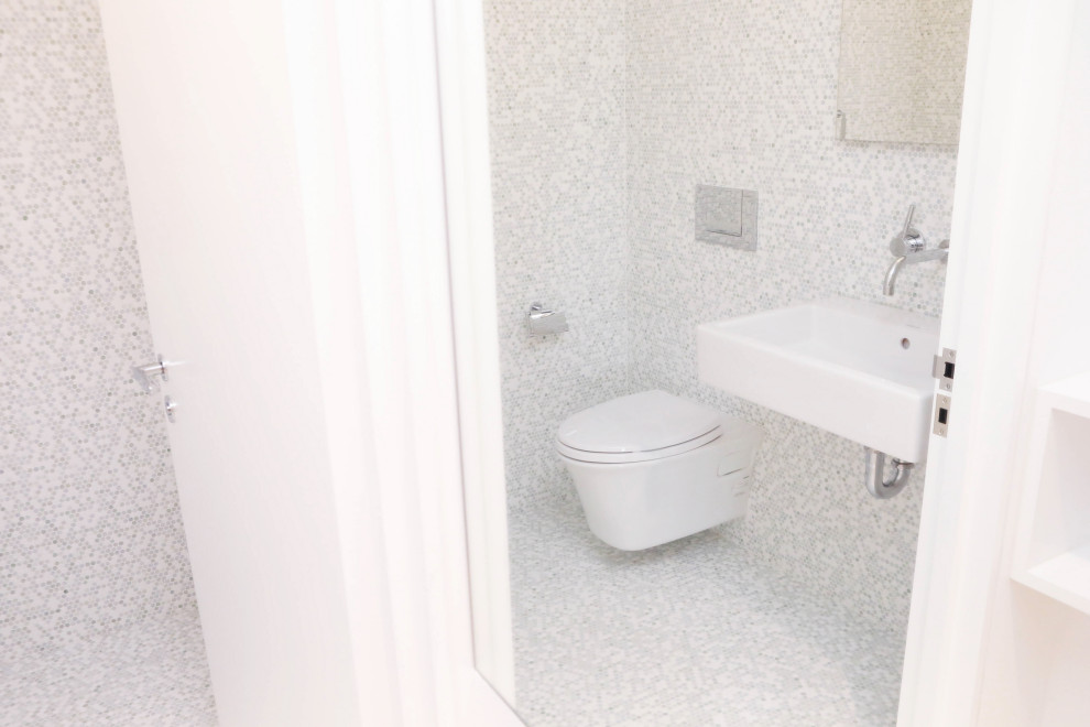 Foto på ett litet funkis badrum för barn, med en vägghängd toalettstol, vita väggar, mosaikgolv, ett väggmonterat handfat och vitt golv