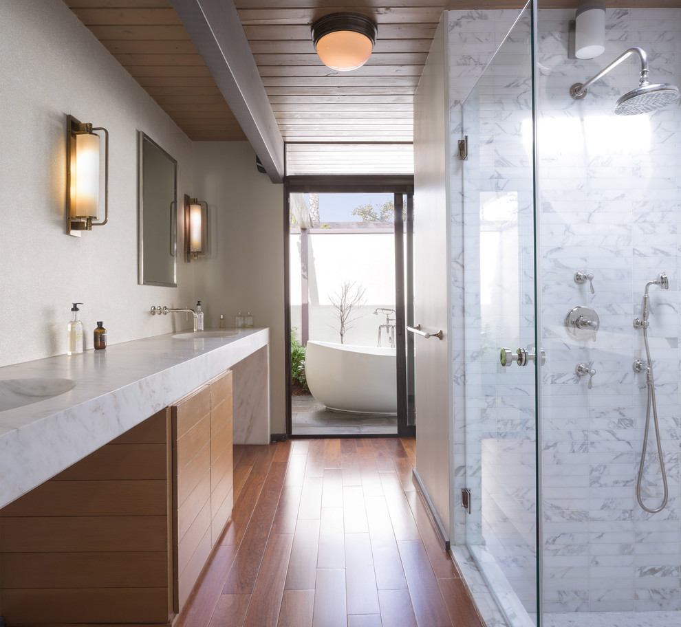 Идея дизайна: большая главная ванная комната в стиле ретро с плоскими фасадами, светлыми деревянными фасадами, отдельно стоящей ванной, душевой комнатой, серой плиткой, мраморной плиткой, бежевыми стенами, паркетным полом среднего тона, монолитной раковиной, мраморной столешницей, коричневым полом, душем с распашными дверями и белой столешницей