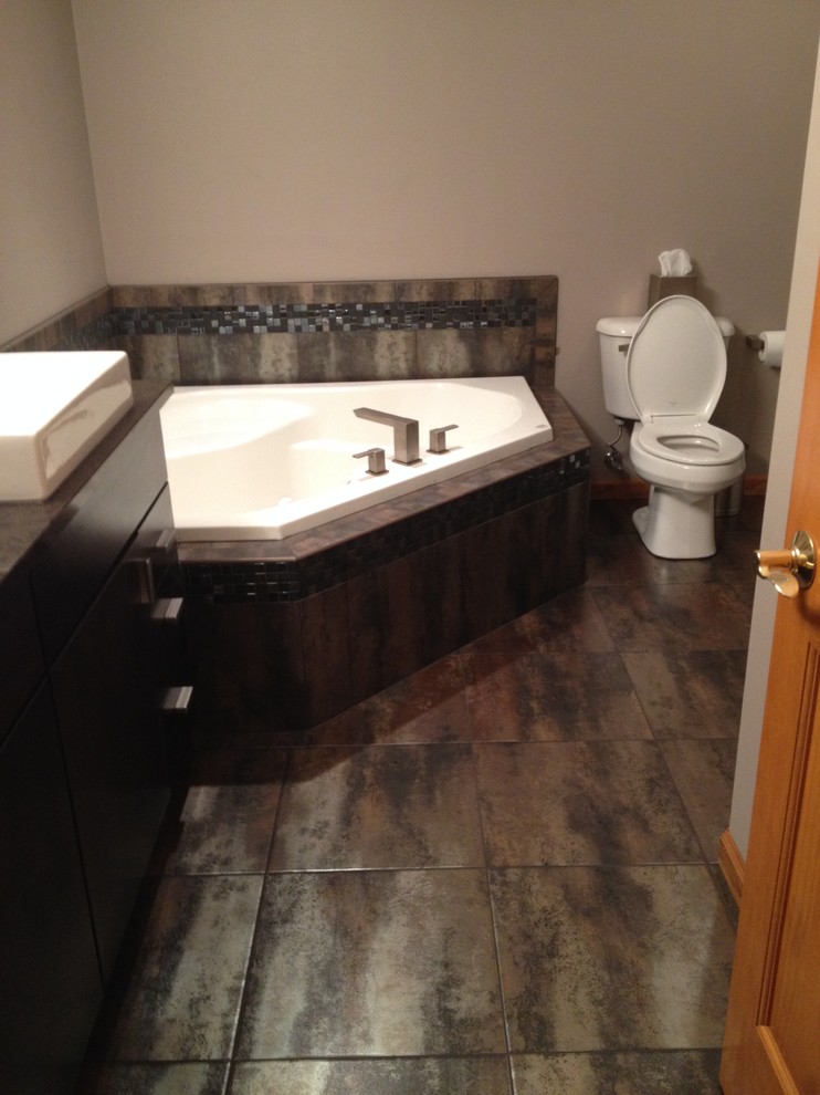 Cette photo montre une salle de bain moderne avec une baignoire d'angle, un carrelage noir, un carrelage marron, un carrelage gris, des carreaux de céramique, un mur beige et un sol en carrelage de céramique.