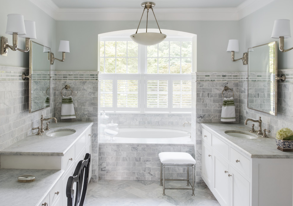 На фото: серо-белая ванная комната в классическом стиле с врезной раковиной, белыми фасадами, полновстраиваемой ванной, серой плиткой, плиткой кабанчик и окном с