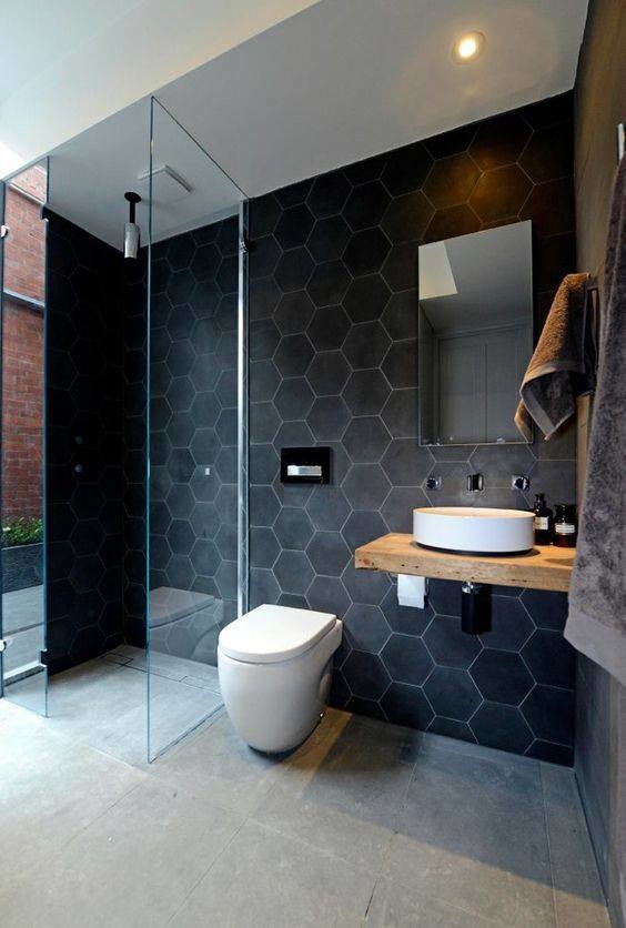 Modern inredning av ett mellanstort badrum med dusch, med öppna hyllor, skåp i ljust trä, en öppen dusch, en toalettstol med hel cisternkåpa, svart kakel, marmorkakel, svarta väggar, betonggolv, ett fristående handfat, träbänkskiva, grått golv och med dusch som är öppen