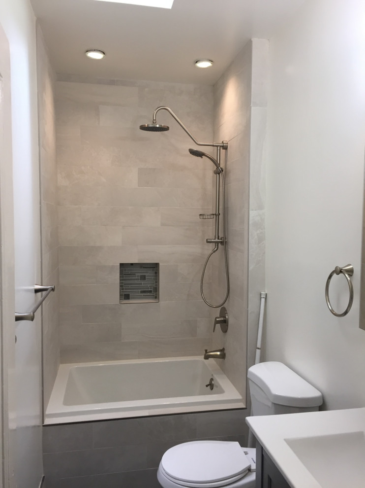 Klassisk inredning av ett mellanstort vit vitt badrum med dusch, med ett badkar i en alkov, en dusch/badkar-kombination, en toalettstol med separat cisternkåpa, grå kakel, porslinskakel, vita väggar, ett undermonterad handfat och bänkskiva i akrylsten