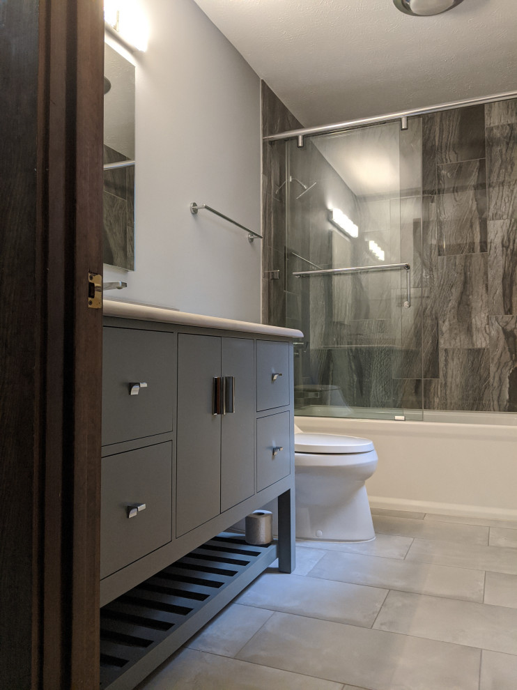 Idée de décoration pour une salle de bain tradition en bois foncé avec une baignoire en alcôve, un combiné douche/baignoire, un carrelage gris, des carreaux de porcelaine, un mur gris, un sol en carrelage de porcelaine, un sol gris, meuble simple vasque, une cabine de douche à porte coulissante et un plan de toilette blanc.