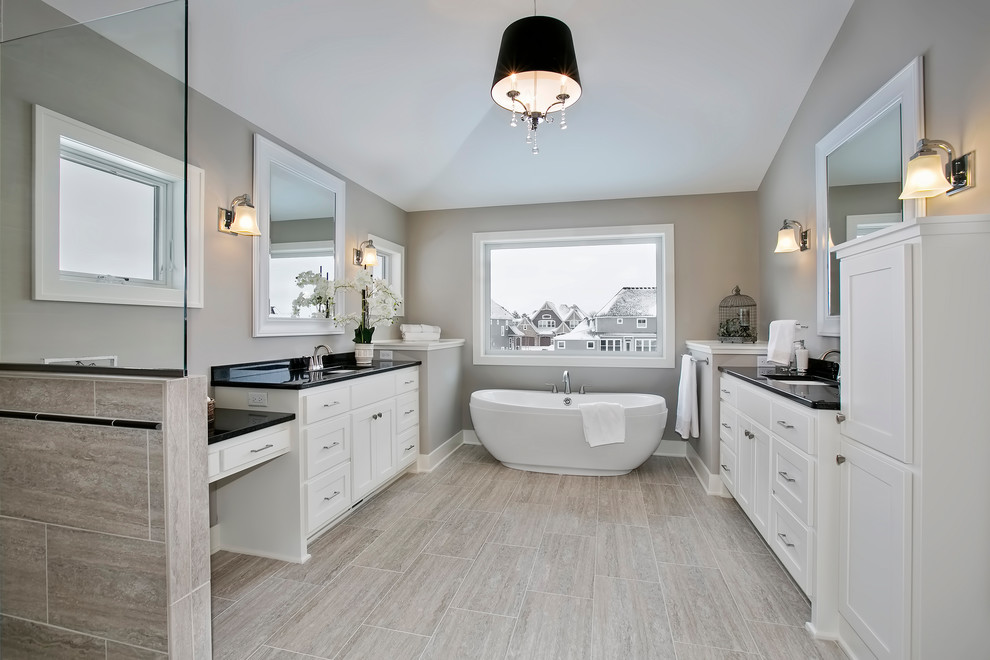 Пример оригинального дизайна: ванная комната в стиле неоклассика (современная классика) с фасадами в стиле шейкер, белыми фасадами, отдельно стоящей ванной, серыми стенами, врезной раковиной, серым полом и черной столешницей