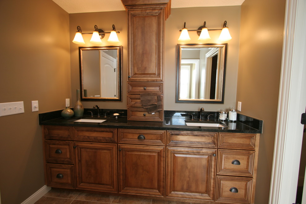 Immagine di una stanza da bagno chic con lavabo sottopiano, ante con bugna sagomata, ante in legno scuro e top in granito