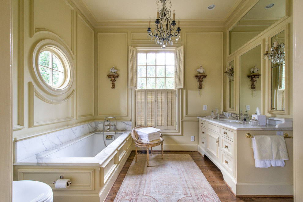 На фото: главная ванная комната в викторианском стиле с бежевыми фасадами, полновстраиваемой ванной, бежевыми стенами, паркетным полом среднего тона, врезной раковиной, мраморной столешницей и коричневым полом