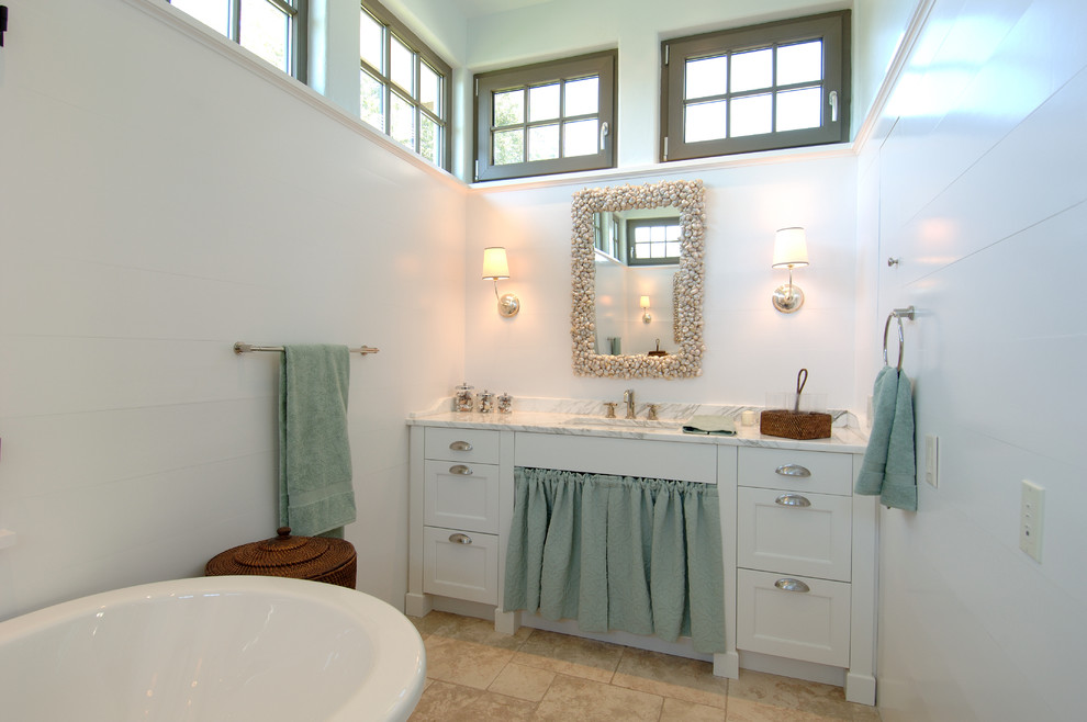 Réalisation d'une grande salle de bain champêtre avec un placard à porte shaker, des portes de placard blanches, une baignoire indépendante, un plan de toilette en marbre, un carrelage beige, une plaque de galets, un mur blanc, un sol en galet et un lavabo encastré.