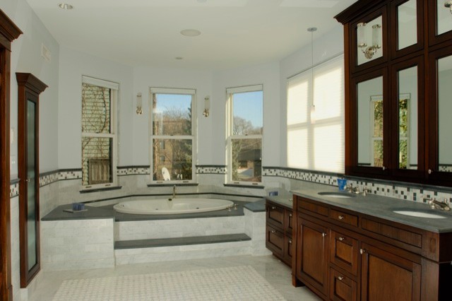 На фото: большая ванная комната в стиле модернизм с фасадами островного типа, фасадами цвета дерева среднего тона, столешницей из оникса, угловой ванной, серой плиткой, керамогранитной плиткой, белыми стенами и полом из керамогранита с