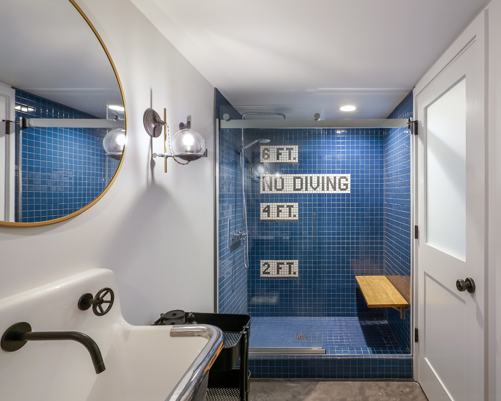 Aménagement d'une salle de bain industrielle avec un carrelage bleu, des carreaux de céramique, un mur blanc, sol en béton ciré, un lavabo suspendu, un sol gris, une cabine de douche à porte coulissante et un banc de douche.