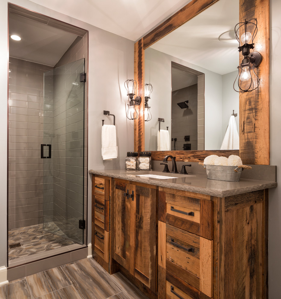 Cette photo montre une douche en alcôve montagne en bois brun avec un placard à porte shaker, un carrelage gris, un mur gris, un lavabo encastré, un sol marron, une cabine de douche à porte battante et un plan de toilette marron.