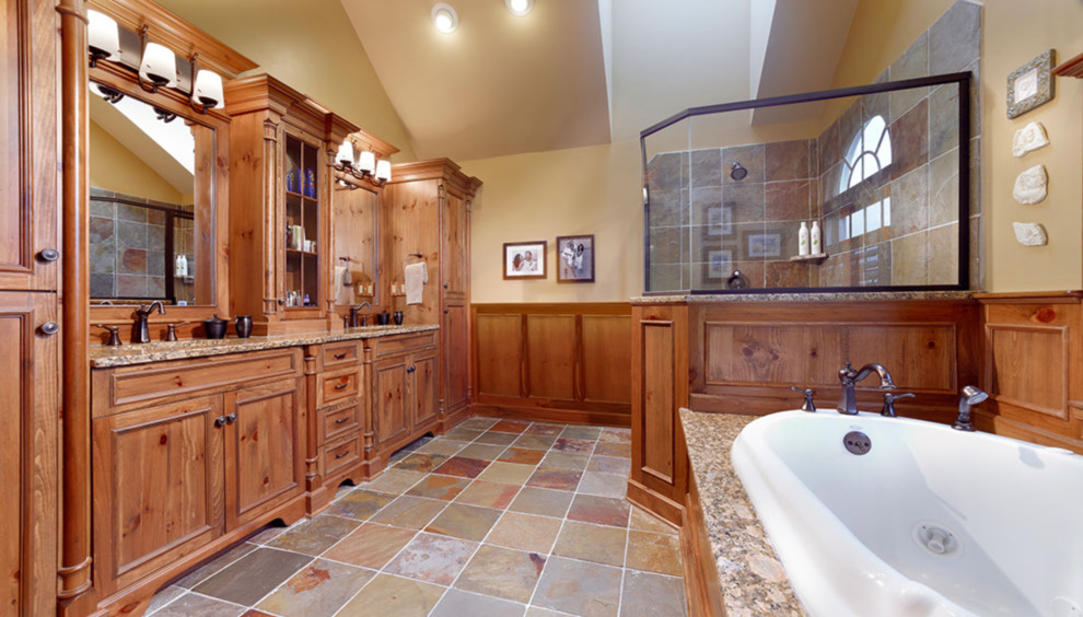 Cette image montre une grande salle de bain principale chalet avec un placard avec porte à panneau encastré, des portes de placard marrons, une baignoire posée, une douche d'angle, un carrelage marron, du carrelage en ardoise, un mur beige, un sol en ardoise, un lavabo encastré, un plan de toilette en granite, un sol multicolore et un plan de toilette marron.