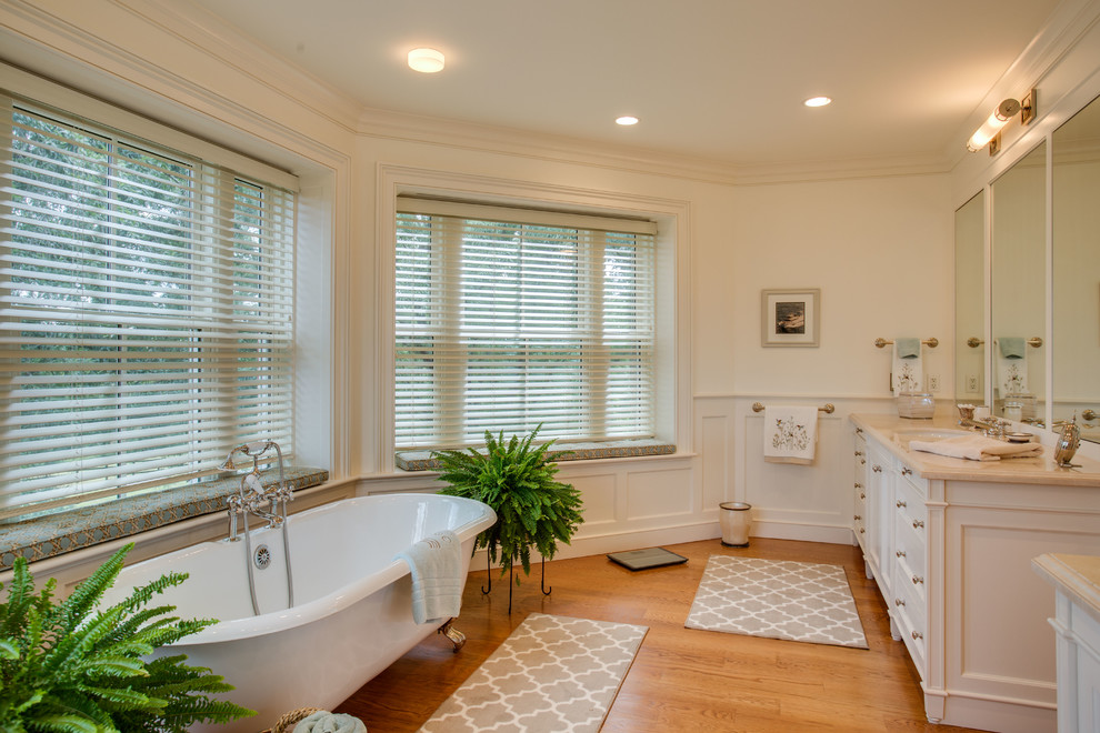 Diseño de cuarto de baño tradicional con lavabo bajoencimera, puertas de armario blancas, bañera con patas y suelo de madera en tonos medios