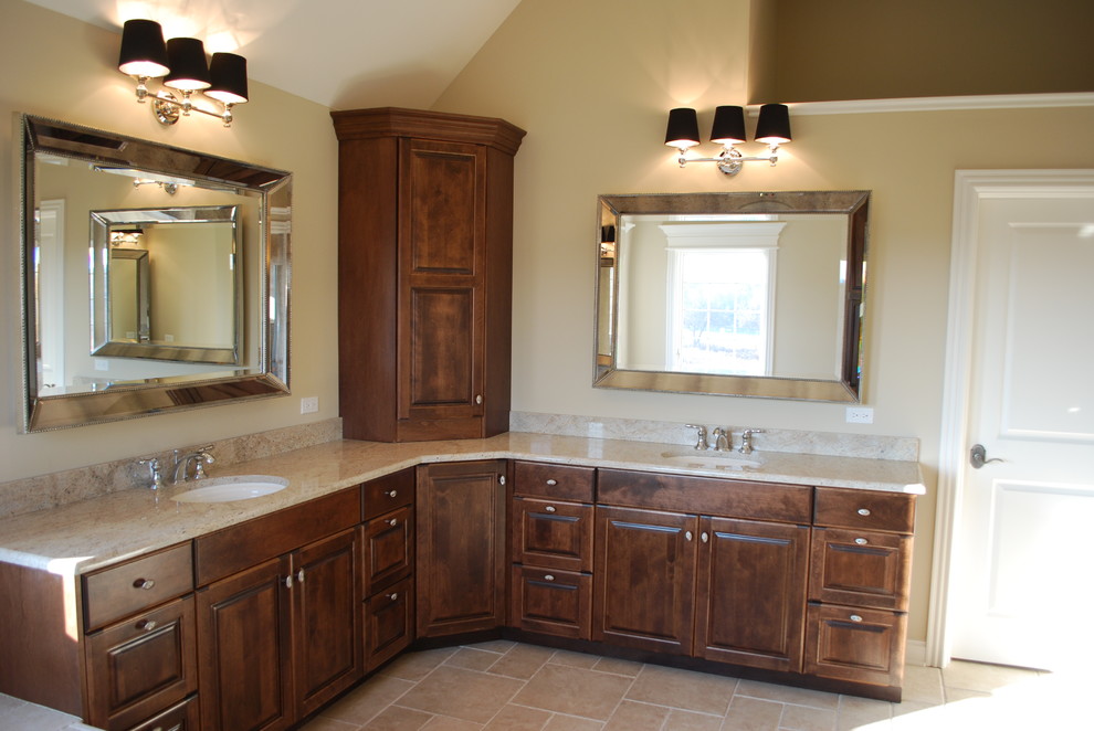 Photo of a traditional bathroom in Chicago with raised-panel cabinets, medium wood cabinets, granite worktops, a corner bath, a walk-in shower, a two-piece toilet, beige tiles, stone tiles, beige walls, limestone flooring and a submerged sink.