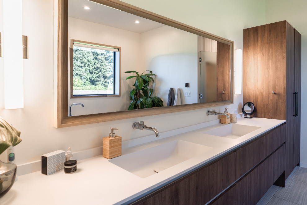 Inspiration for a large modern ensuite bathroom in Portland with flat-panel cabinets, light wood cabinets, a wall mounted toilet, white walls, an integrated sink, solid surface worktops, grey floors, white worktops, a floating vanity unit, double sinks and porcelain flooring.