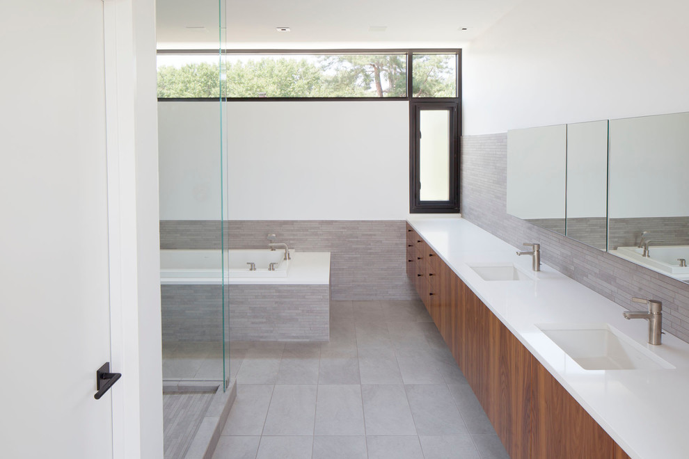 Immagine di una stanza da bagno minimalista con lavabo sottopiano, ante lisce, ante in legno scuro, vasca da incasso, doccia ad angolo, piastrelle grigie, piastrelle a listelli, pareti bianche e pavimento grigio
