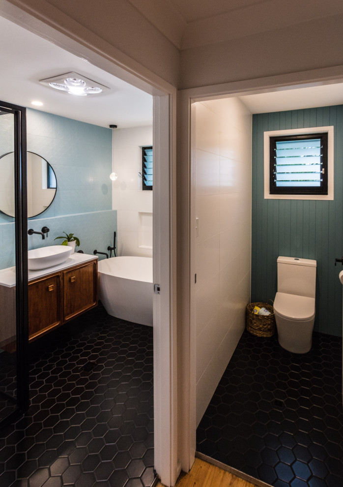 Small 1950s kids' blue tile and porcelain tile ceramic tile and black floor bathroom photo in Sydney with furniture-like cabinets, medium tone wood cabinets, a one-piece toilet, white walls, a vessel sink, quartz countertops, a hinged shower door and white countertops