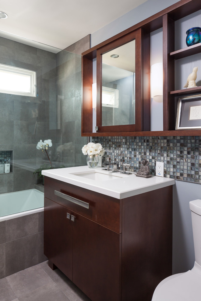 Exemple d'une petite salle de bain tendance en bois foncé avec un lavabo encastré, un combiné douche/baignoire, mosaïque, un placard à porte plane, une baignoire indépendante, un mur gris, un sol en carrelage de porcelaine, WC séparés et un carrelage gris.