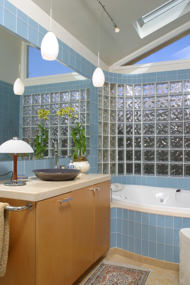 На фото: главная ванная комната в стиле ретро с плоскими фасадами, синей плиткой, стеклянной плиткой, полом из известняка, настольной раковиной, столешницей из известняка, светлыми деревянными фасадами, накладной ванной, серыми стенами и коричневым полом с