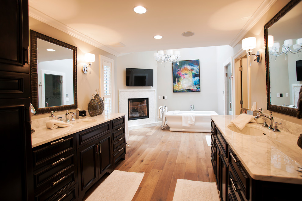 This is an example of a large traditional ensuite bathroom in Miami with raised-panel cabinets, dark wood cabinets, a freestanding bath, beige walls, light hardwood flooring, a submerged sink and marble worktops.