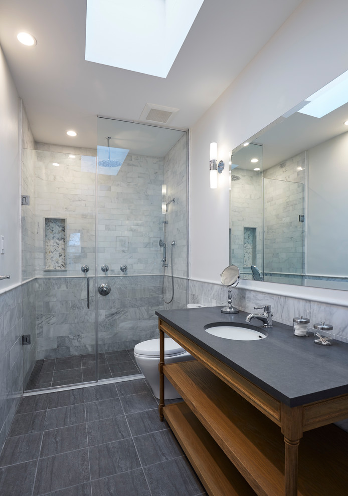 Inspiration for a large transitional master gray tile and marble tile porcelain tile and black floor walk-in shower remodel in New York with open cabinets, medium tone wood cabinets, a one-piece toilet, white walls, an undermount sink, a hinged shower door, soapstone countertops and gray countertops
