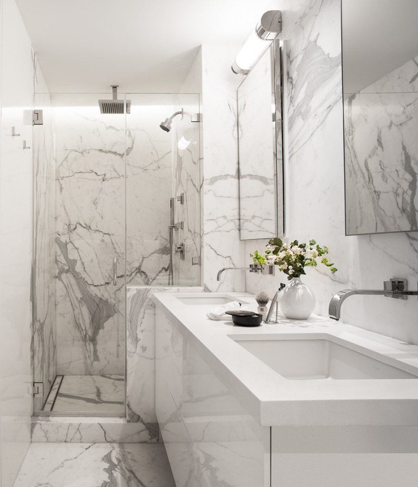 Inredning av ett modernt mellanstort vit vitt badrum med dusch, med ett undermonterad handfat, släta luckor, vita skåp, en dusch i en alkov, vita väggar, vit kakel, marmorkakel, marmorgolv, bänkskiva i akrylsten, grått golv och dusch med gångjärnsdörr
