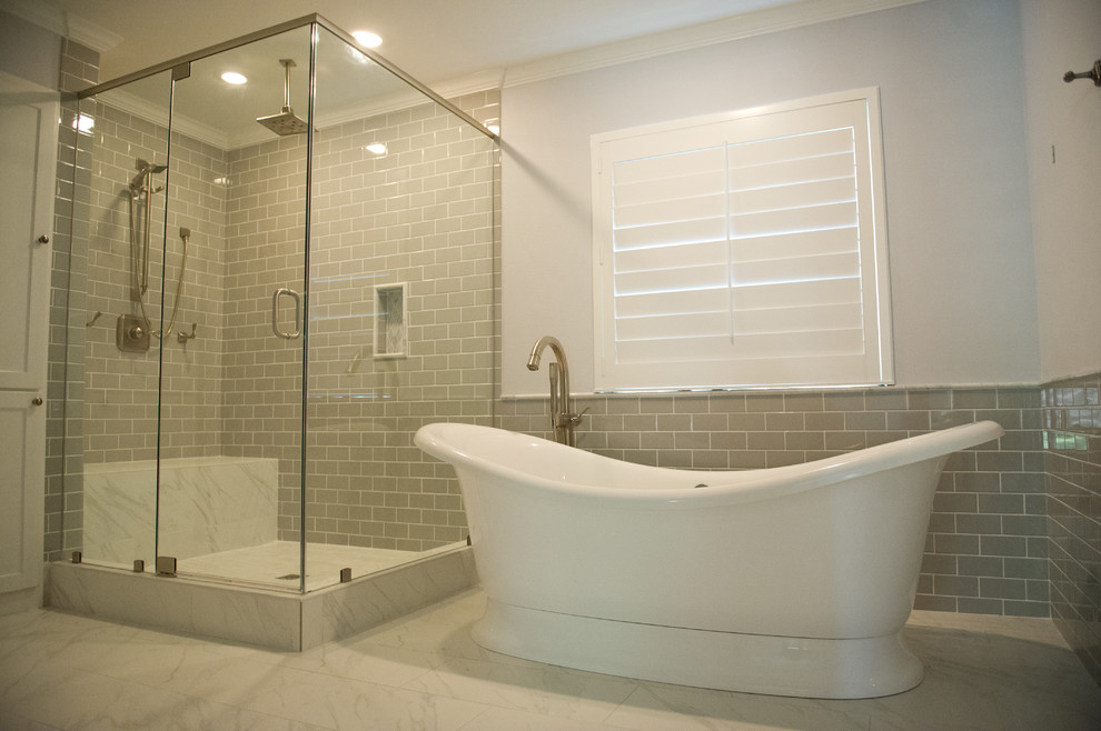 Cette image montre une salle de bain minimaliste avec des portes de placard blanches, un plan de toilette en granite, une baignoire indépendante, une douche ouverte, un carrelage gris, un carrelage métro et un sol en marbre.